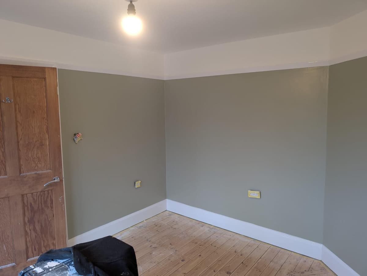 Room freshly painted in sage green with white skirting boards